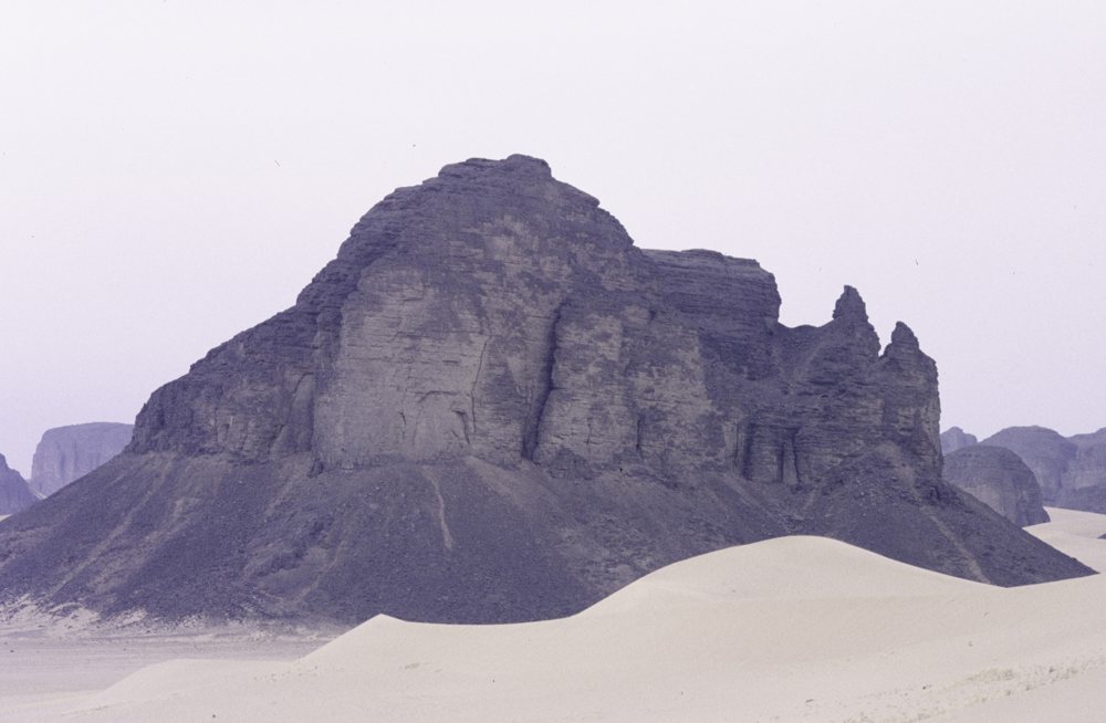 <div class='fn'> Towering rocks behind desert sand dunes - Afara, Algeria - F…