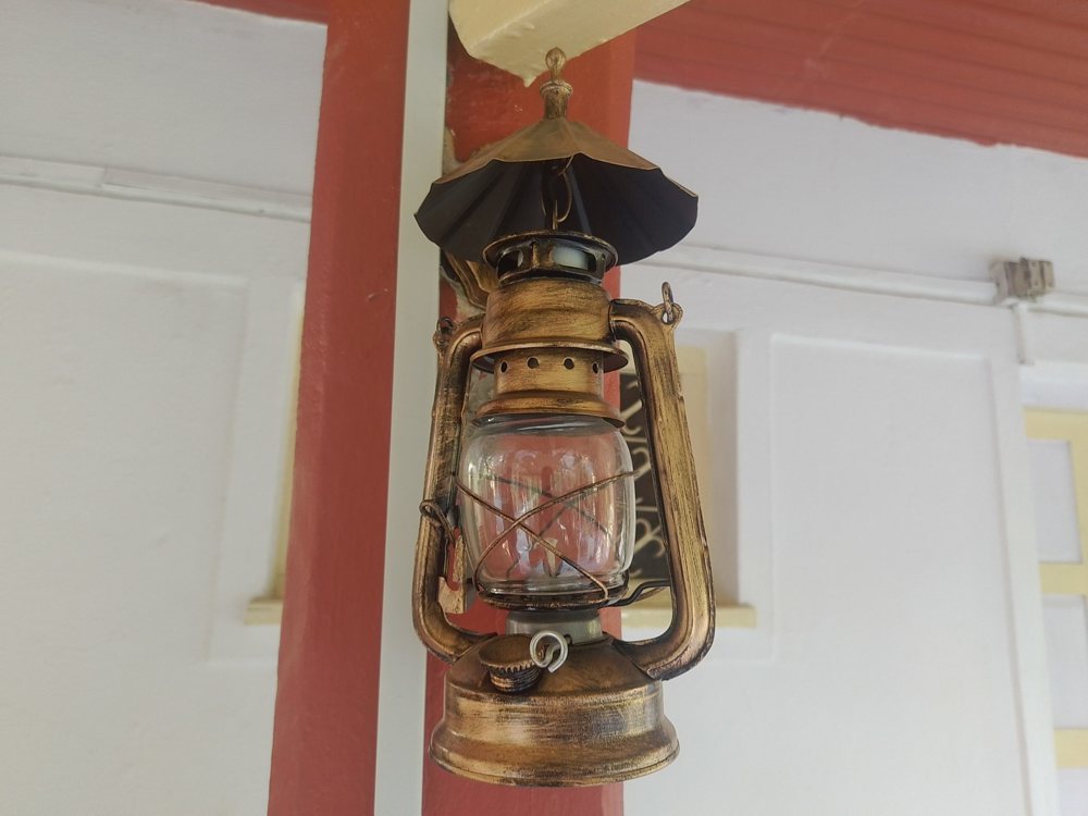 A vintage oil lantern hangs from a ceiling, featuring a metallic body with a …