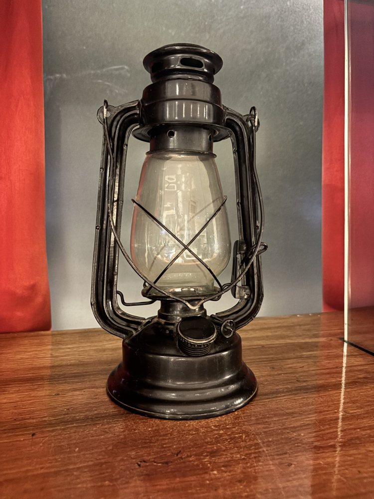 A vintage oil lantern is displayed on a wooden surface.